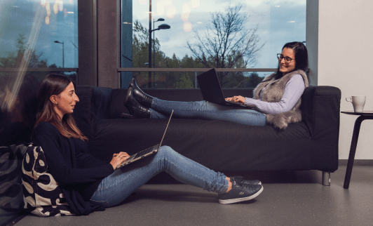 Two coworkers seated socializing and smiling with computers on their laps